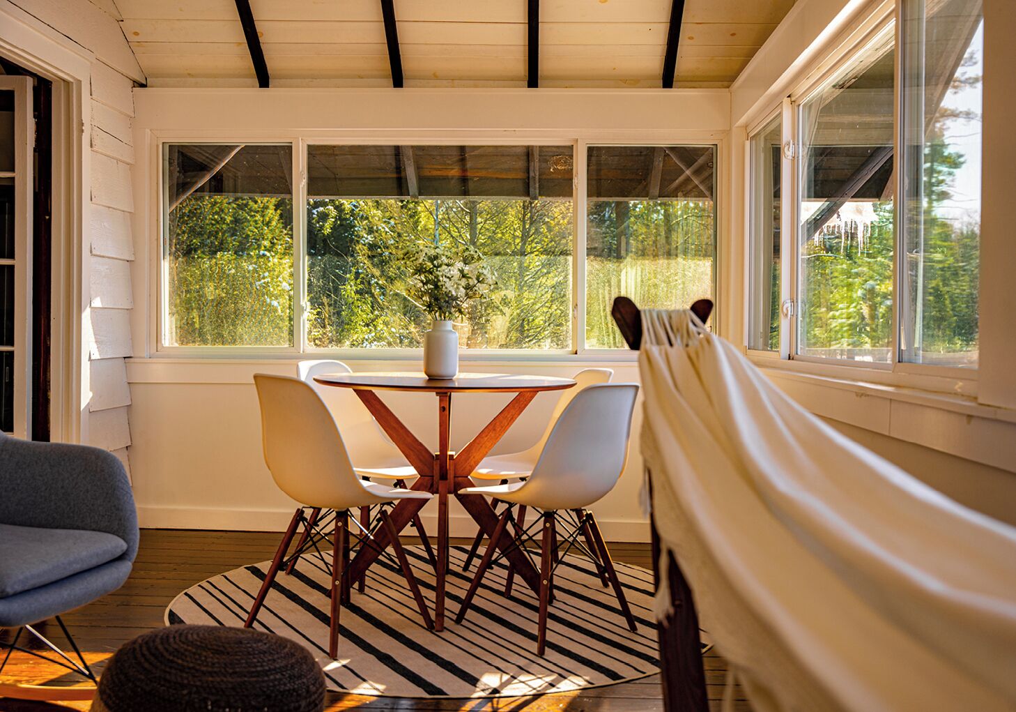 A sunlit room with a table and chairs, a window with a view of trees, and a hammock.