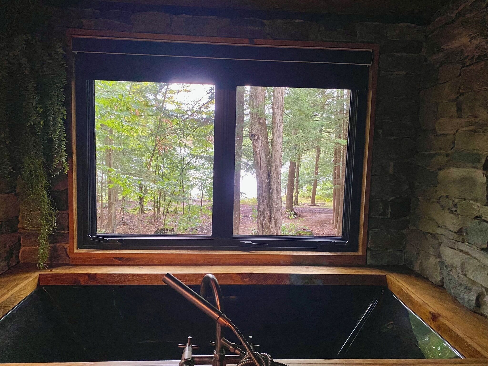 A stone wall, a window with a view of a forest, and a bathtub with a faucet.