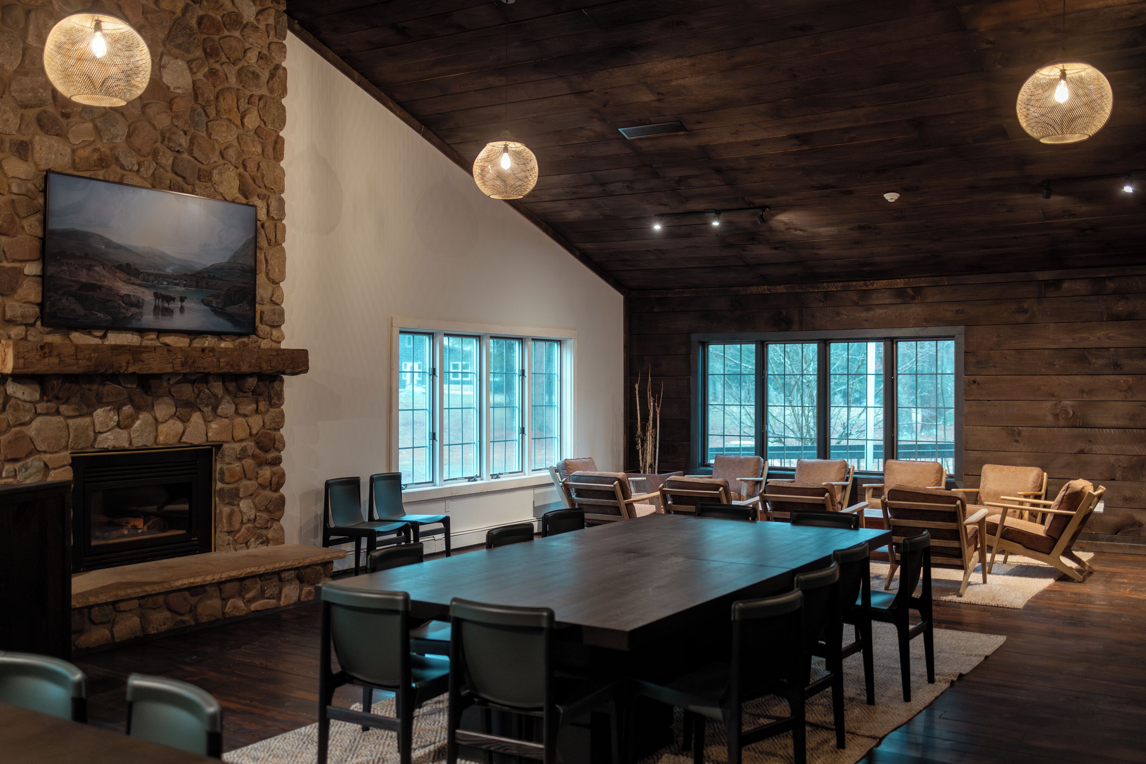 A spacious room with a large table, chairs, a fireplace, and large windows.