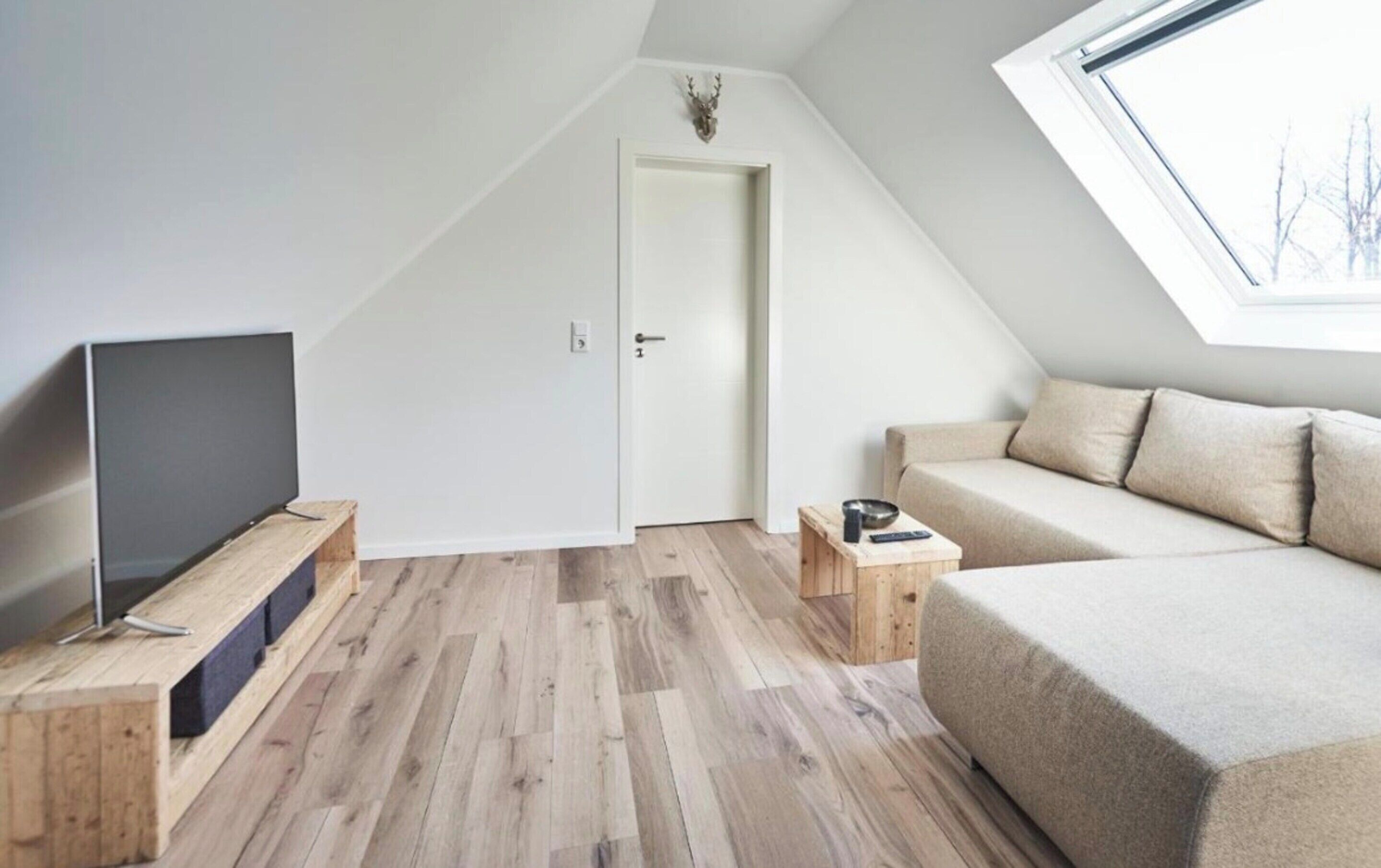 A modern loft bedroom with a sloped ceiling, a television on a wooden stand, a sofa, and a small table with a remote.