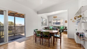 Un'ampia stanza con pavimento in legno, un tavolo da pranzo con sedie, un divano e un balcone con ringhiera in legno.