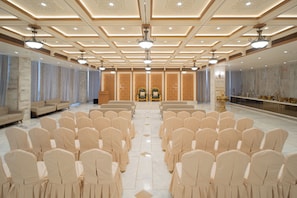 A spacious hall with rows of chairs, a podium, and a decorative wall with a statue. - STATUS DINE BANQUET AND RESTAURANT (Ahmedabad)