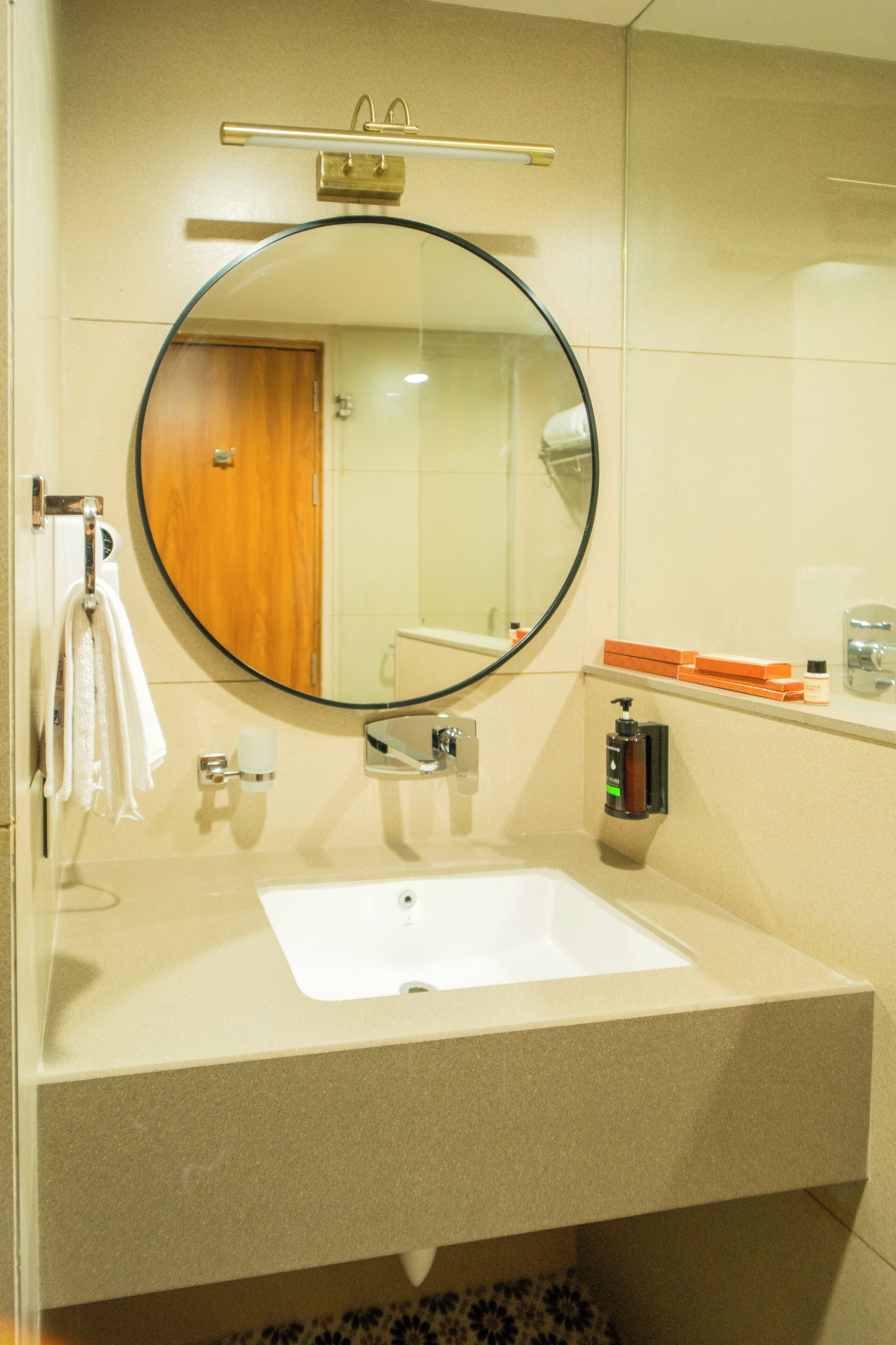 A bathroom with a round mirror, a white sink, a towel rack, and toiletries on the wall.