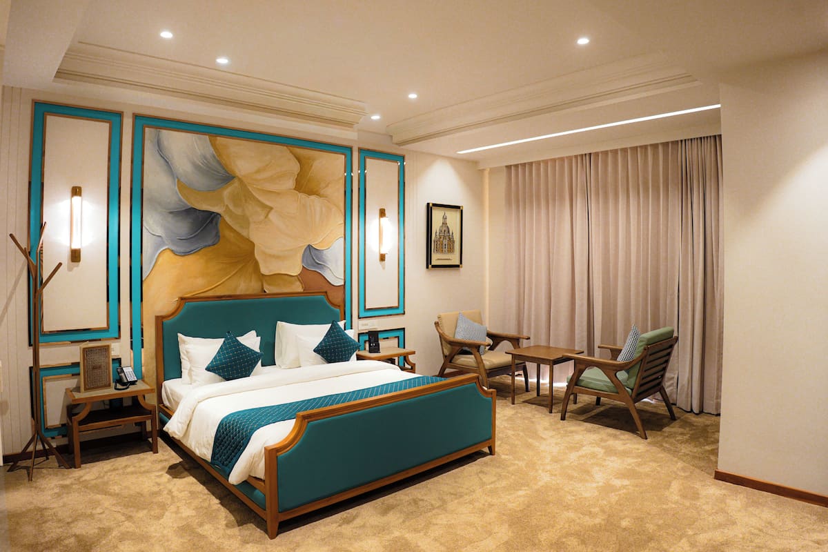 A hotel room with a large bed, two chairs, a small table, and a painting on the wall.