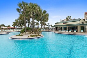 A swimming pool with lounge chairs, palm trees, and a building with a green roof. - Luxury 3BR Beachfront Condo Sleeps 8 Gulf Views (Panama City Beach)
