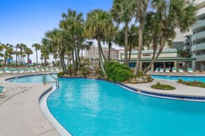 A swimming pool with a curved design, surrounded by palm trees and lounge chairs. - Luxury 3BR Beachfront Condo Sleeps 8 Gulf Views (Panama City Beach)