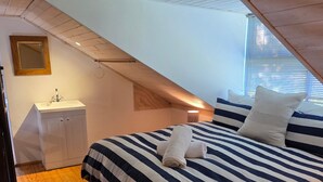 Une chambre avec un plafond en pente, un lit avec une literie à rayures, une table de chevet et un miroir.