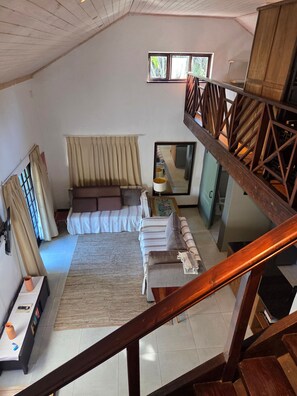 A room with a bed, a sofa, a window, a mirror, and a staircase. - Loft Cottage - Knysna (Knysna)