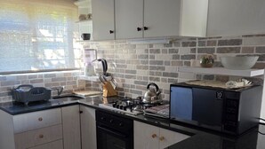 Une cuisine moderne avec des meubles blancs, un plan de travail noir, un four encastré, une bouilloire et un four à micro-ondes.