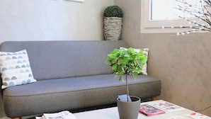 A grey sofa with a cushion, a grey pot with a plant, and a table with magazines and papers.