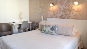A hotel room with a bed, a desk, a chair, and a wall with a leaf pattern.