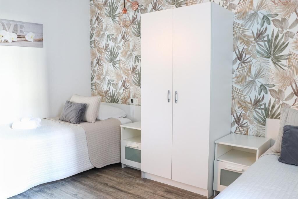 Una camera da letto con un letto, un armadio, un comodino e una parete decorata con un motivo a foglia tropicale.