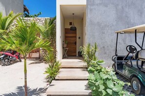 A pathway leading to a wooden door, surrounded by greenery and a golf cart. - Luxury Ocean View Condo (Isla Mujeres)