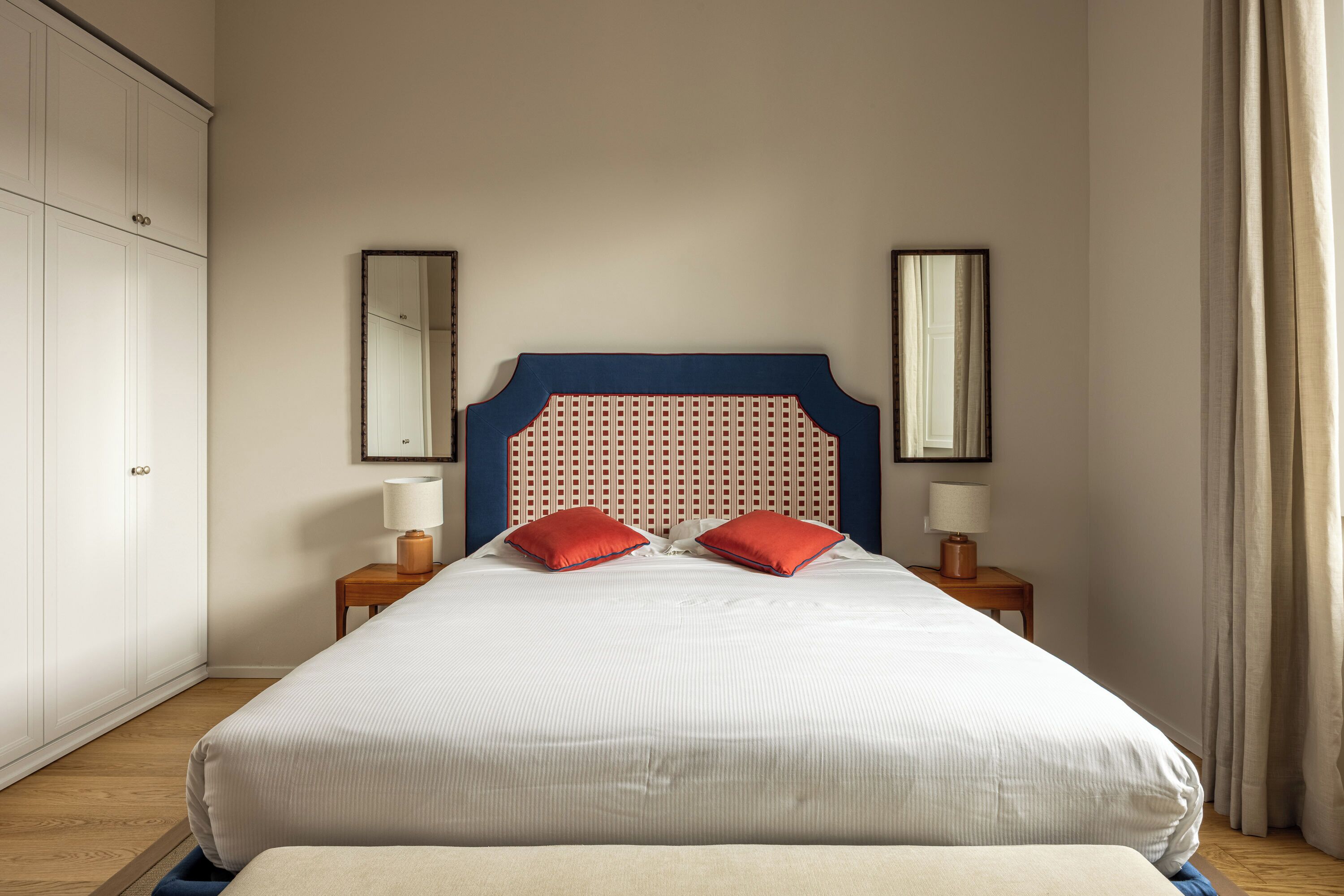A bedroom with a large bed, two nightstands, a wardrobe, and two wall mirrors.