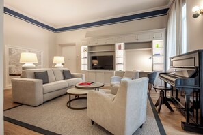 Un salon comprenant un canapé, des fauteuils, une table basse, un piano et des étagères intégrées.