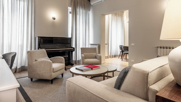 Un salon comprenant un piano, deux fauteuils, un canapé, une table basse et une lampe.