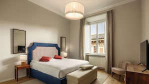 Une chambre à coucher avec un lit, des tables de chevet, une télévision, une fenêtre avec des rideaux et une vue sur un bâtiment à l’extérieur.