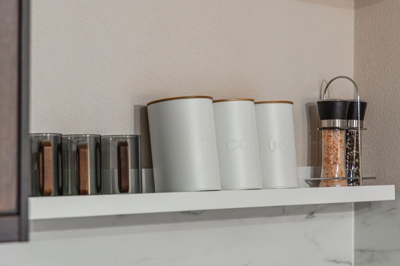 A white shelf with various containers, including a salt shaker and a pepper shaker.