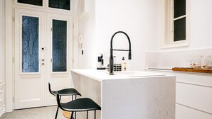 Moderni keittiö, jossa on valkoiset kaapit, keskellä oleva keittiösaareke, mustat tuolit ja ikkuna.