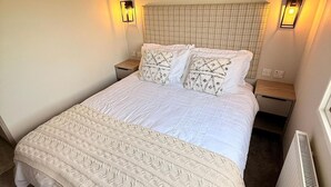 A single bed with a quilted white bedspread, two matching pillows, two bedside tables with lamps, and a radiator. - 3-bed - Sleeps 6 - Parking - Balcony (Malton)