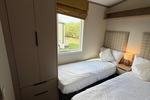 A bedroom with two beds, a wardrobe, a window with a view of greenery, and a bedside lamp. - 3-bed - Sleeps 6 - Parking - Balcony (Malton)