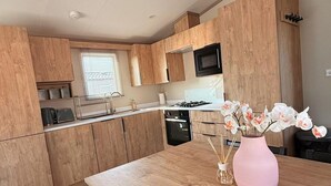 A modern kitchen with wooden cabinets, a gas stove, and a pink vase with flowers on the table. - 3-bed - Sleeps 6 - Parking - Balcony (Malton)