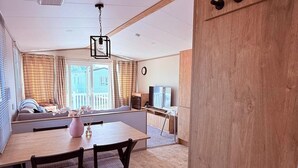 A living room with a wooden dining table, chairs, a TV, and a sofa. - 3-bed - Sleeps 6 - Parking - Balcony (Malton)