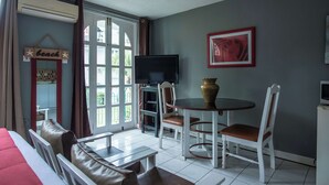 Un salon comprenant un canapé, un téléviseur, une table à manger avec des chaises, un vase et un tableau accroché au mur.