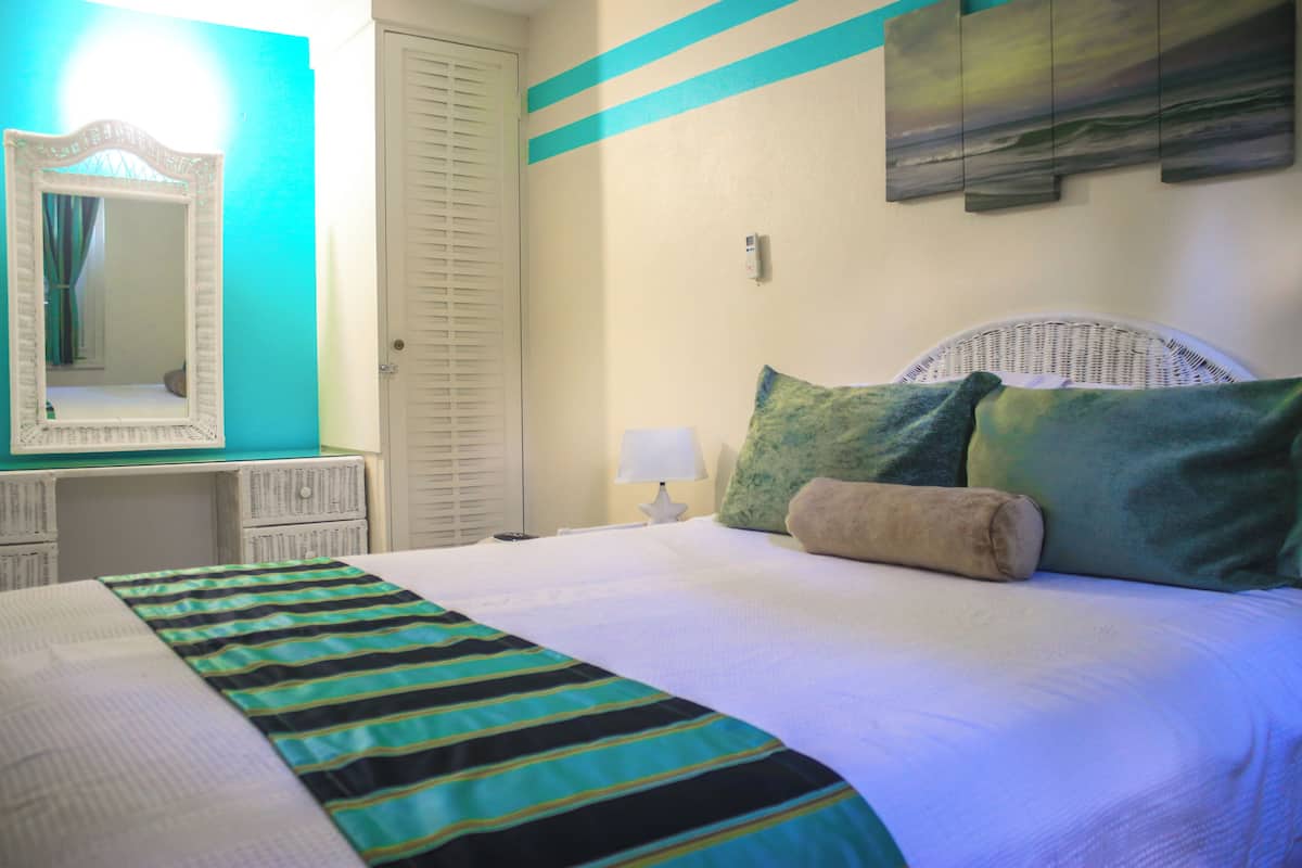 Una habitación de hotel con cama, mesita de noche, espejo, lámpara y una obra de arte colgada en la pared.