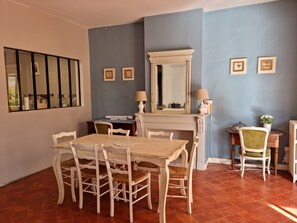 A dining area with a table and chairs, a fireplace, a mirror, and framed pictures on the wall.