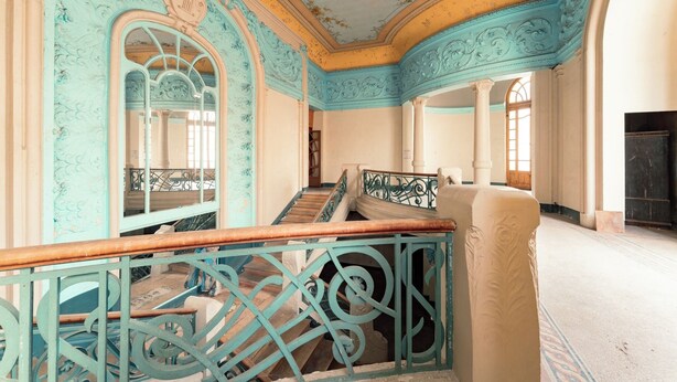 Interior ornamentado com escadaria, molduras decorativas e um espelho grande.