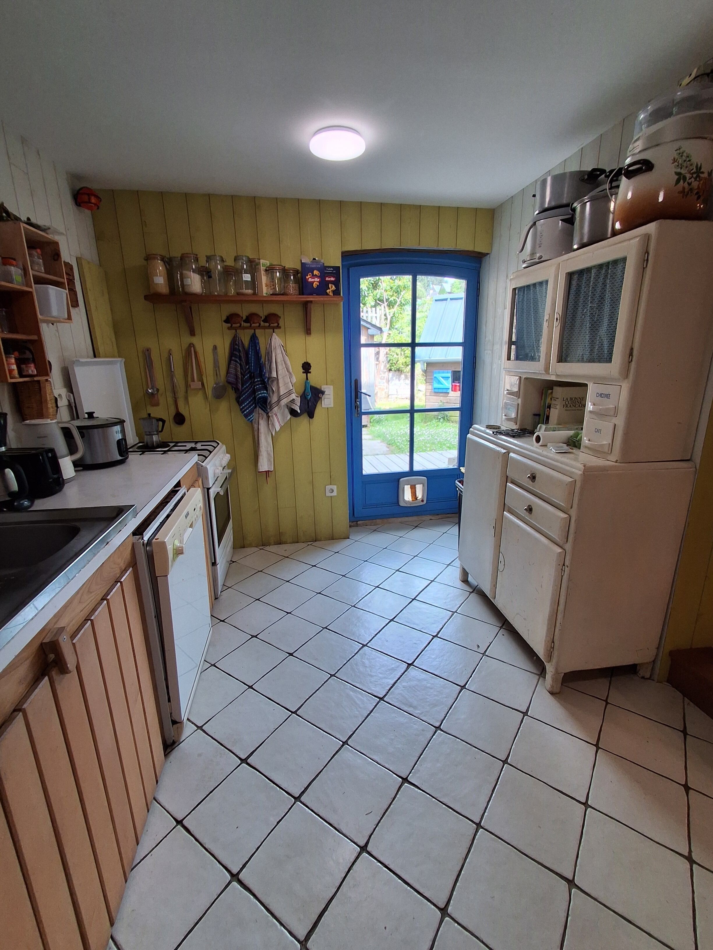 Une cuisine avec une porte bleue, des placards blancs et un sol carrelé.