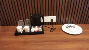 A breakfast setup with a coffee maker, cups, and a plate with cutlery on a wooden table. - Murugammal Residency (Tirupattur)