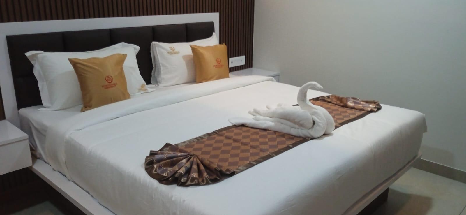 A neatly made bed with a swan-shaped towel and checkered blanket, white pillows, and a headboard with vertical lines.