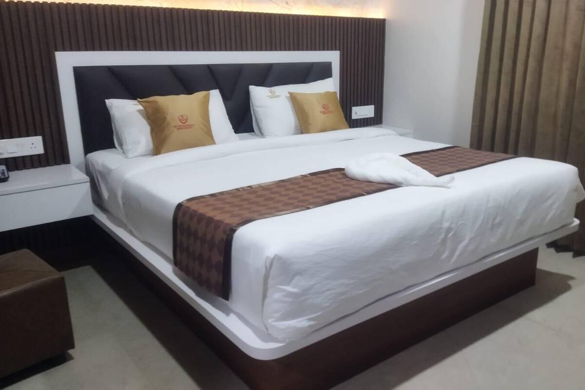 Een hotelkamer met een groot bed, een nachtkastje en een bruin poef.