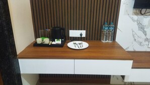 A wooden counter with a coffee maker, a tray with cups and a spoon, a plate with cutlery, and water bottles. - Murugammal Residency (Tirupattur)