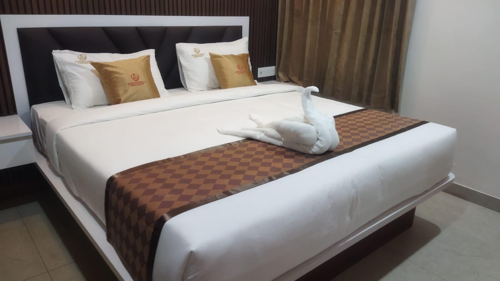 Cama bem arrumada com toalha em formato de cisne, manta xadrez e dois travesseiros com logotipos.