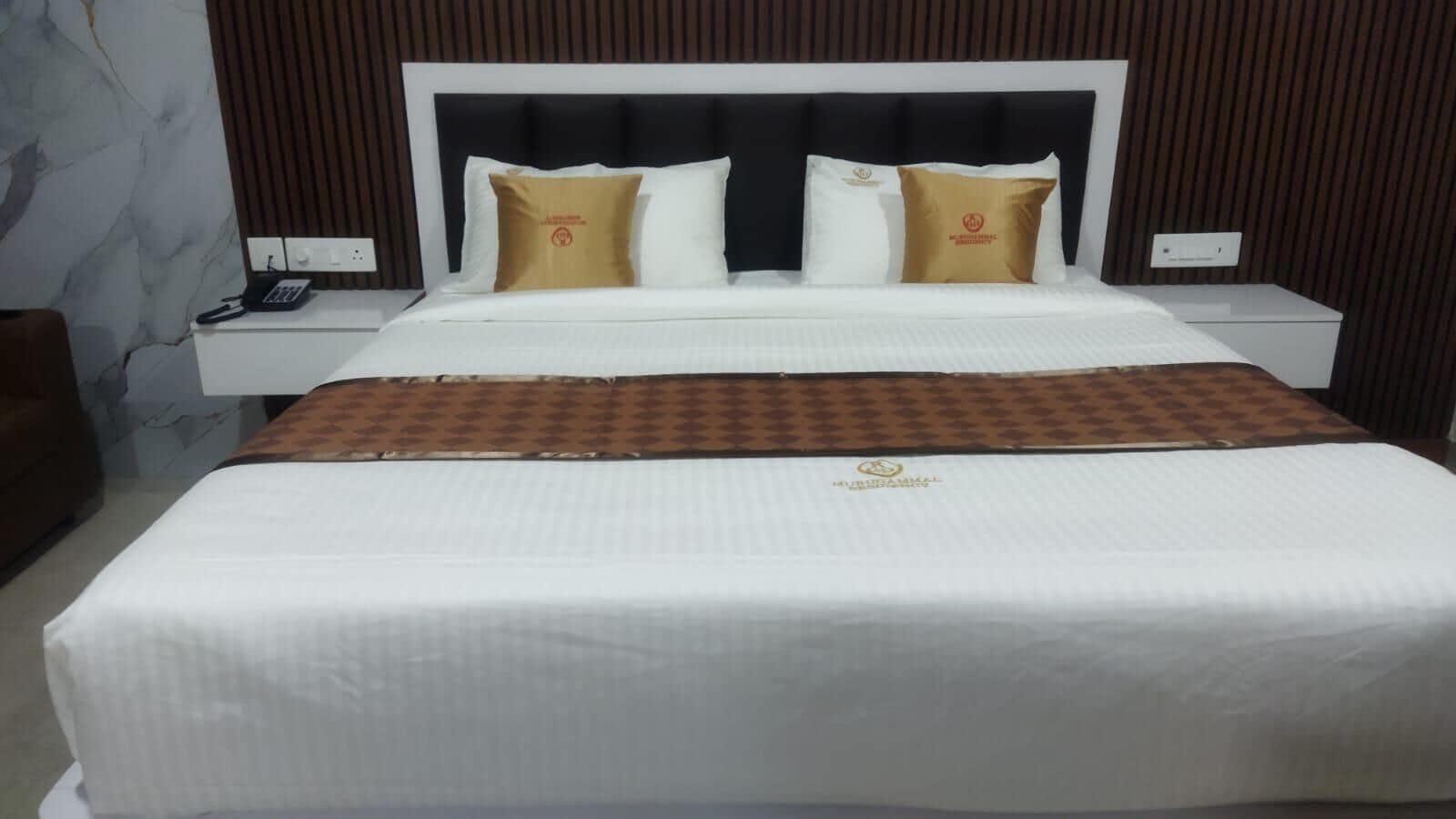 A hotel room with a large bed, a nightstand with a phone, and a marble wall.
