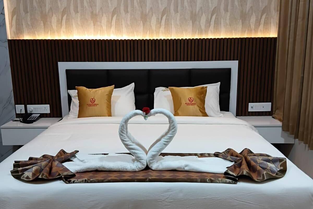 Een hotelkamer met een groot bed, een handdoek gedecoreerd in de vorm van een hart, en een kamer met een patroon op de muur.