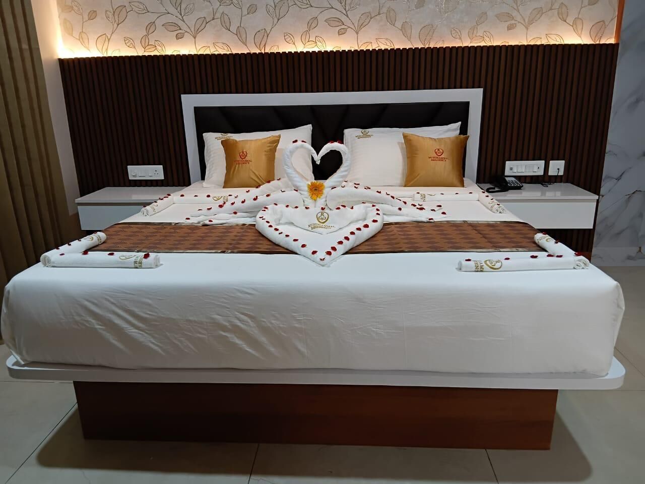 A hotel room with a neatly made bed, a heart-shaped towel arrangement, and a bed with a white headboard.