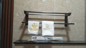 A bathroom with two towels hanging on a rack, a bottle of lotion, and a dental kit on the counter. - Murugammal Residency (Tirupattur)