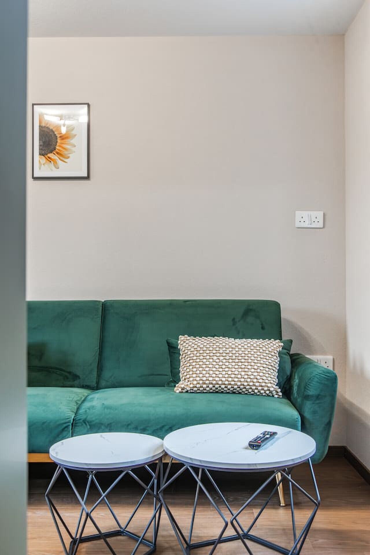 Un sofá verde con un cojín estampado, dos mesitas redondas de metal y un cuadro de un girasol en la pared.