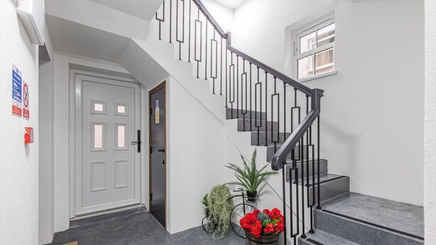Una escalera de diseño moderno, una puerta blanca y un ventanal pequeño.