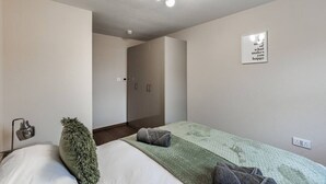 Un dormitorio con cama, una lámpara de noche, un cojín verde decorativo, un aplique en la pared y una cita inspiradora en la pared.