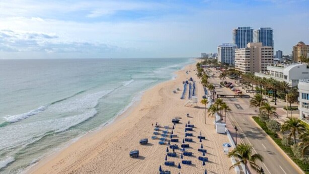 Una playa con filas de tumbonas y un paisaje urbano al fondo.