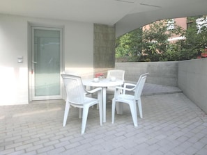 A patio with a table and chairs, a door, and a view of greenery. - Bright Residence Close to the the Beach (Lignano Sabbiadoro)