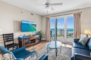 A living room with a TV, sofa, and a balcony with a view. - ☀️Walk to Beach | Gulf Views | 3 Pools | Ariel Dunes II 1507☀️ (Miramar Beach)