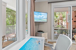 Ein Zimmer mit Fernseher, einem Bild von einem schwimmenden Seestern, einem Essbereich mit Stühlen und Blick auf einen Balkon mit Gartenmöbeln.