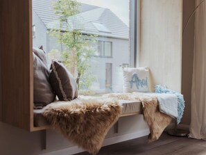 A cozy seating area with a fur throw, pillows, and a window with a view of a building and trees. - 4 Star Holiday Home in Sagad (Sagard)