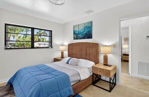 A bedroom with a bed, nightstands, a window with a view, a painting, and a door leading to another room. - Waterfront pool home- 3BR/3BA Hollywood Beach (Hollywood)